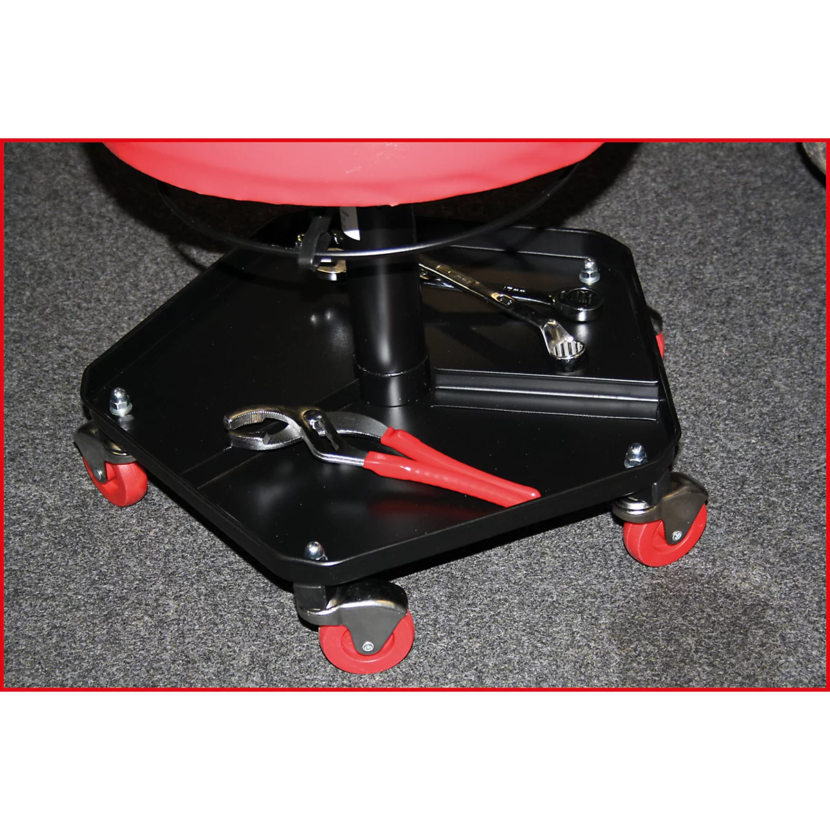 Un tabouret d'atelier noir avec un siège rouge, quatre roues rouges et un plateau avec des outils.